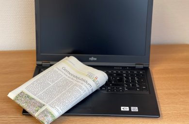 Das Foto zeigt einen aufgeklappten Laptop, auf dessen Tastatur eine gefaltete Zeitung liegt.
