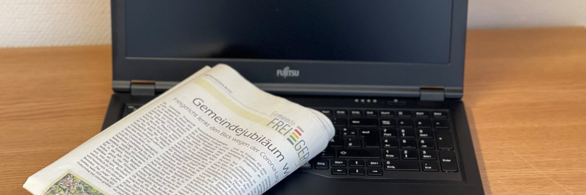 Das Foto zeigt einen aufgeklappten Laptop, auf dessen Tastatur eine gefaltete Zeitung liegt.