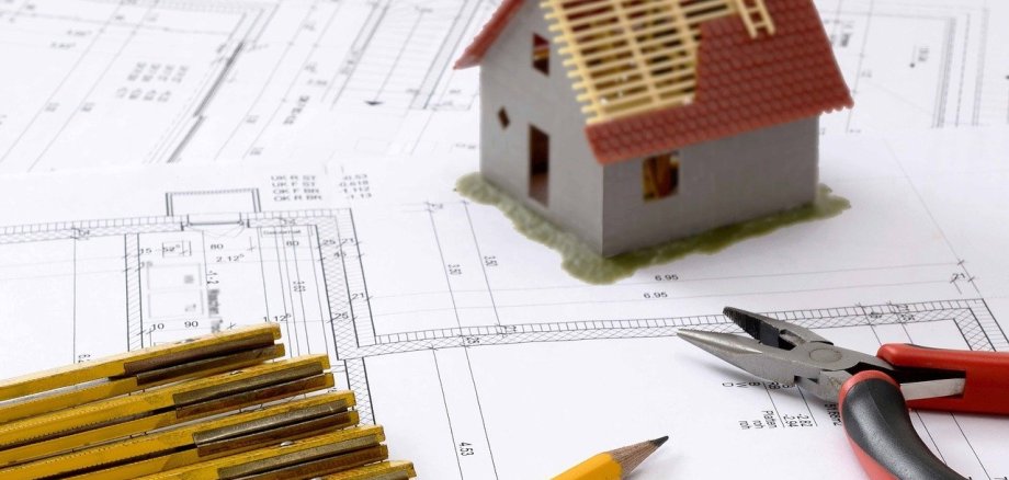 Foto eines Bauplans mit einem Hausmodell einem Stift einer Zange und einem Zollstock