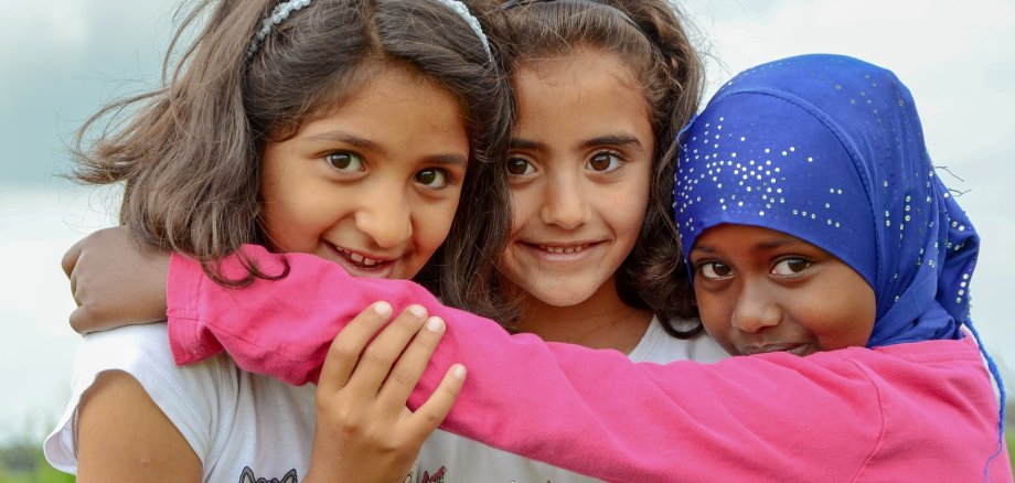 Das Foto zeigt drei sich umarmende Flüchtlingsmädchen.