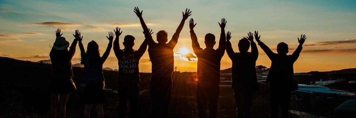 Das Foto zeigt Freunde die sich mit gehobenen Armen und voller Freude den Sonnenuntergang anschauen
