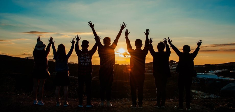 Das Foto zeigt Freunde die sich mit gehobenen Armen und voller Freude den Sonnenuntergang anschauen