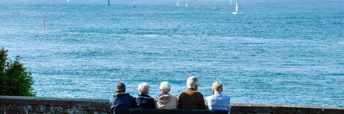 Das Foto zeigt Senioren die auf einer Bank die auf das Meer blicken