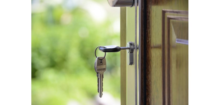 Foto von einem Schlüsselbund wovon ein Schlüssel in einem Türschloss steckt
