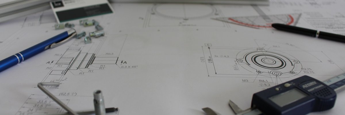 Foto eines Bauplans mit Messschieber, Kugelschreiber, Geodreieck und Imbusschlüssel
