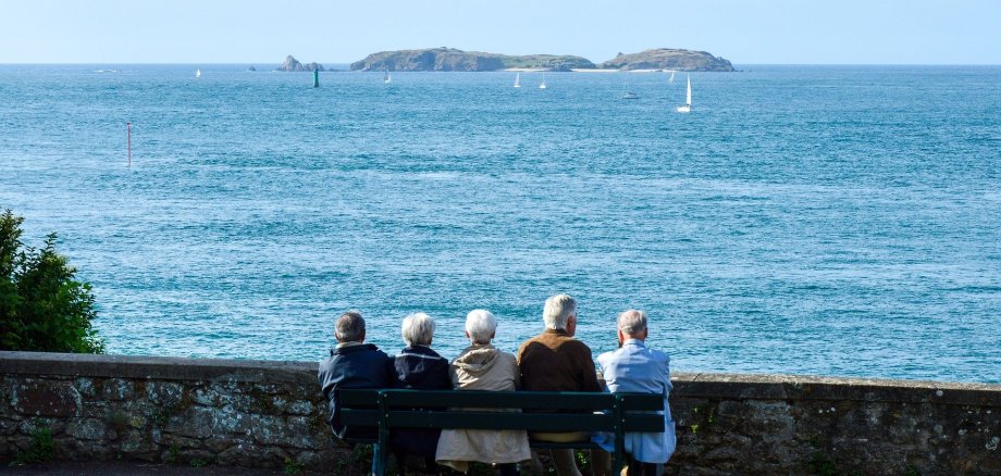 Das Foto zeigt Senioren, die auf einer Bank am Meer sitzen.