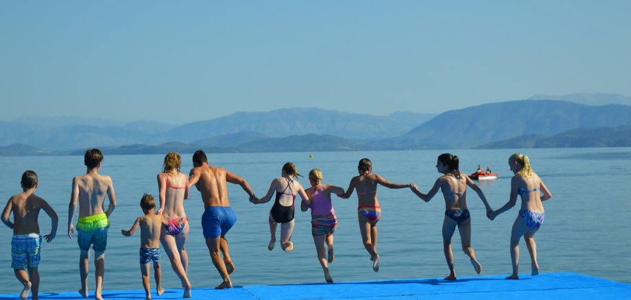 Das Foto zeigt Leute, die zusammen am Strand Hand in Hand ins Meer rennen.