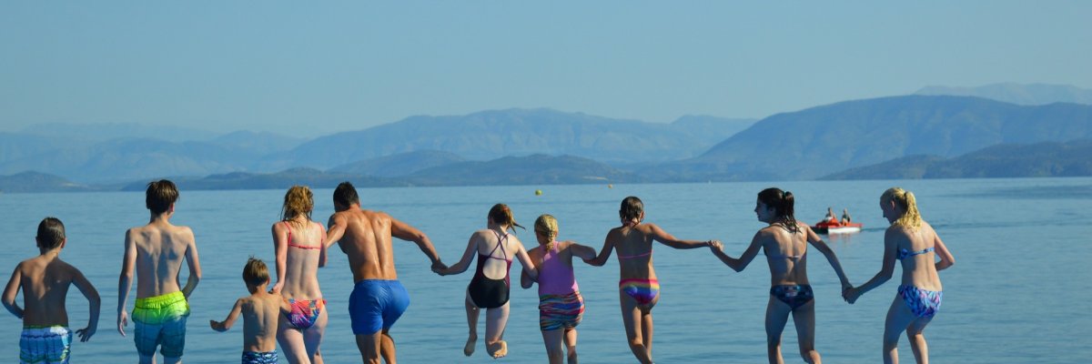 Das Foto zeigt Leute, die zusammen am Strand Hand in Hand ins Meer rennen.