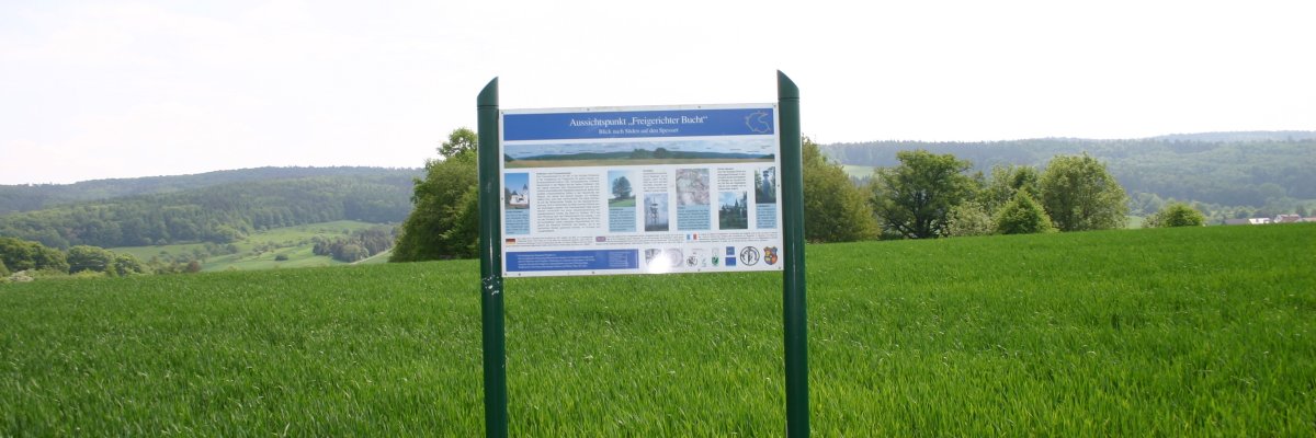 Foto mit einer Informationstafel über den Kulturweg mit einer Ruhebank im Vordergrund auf einer Wiese.