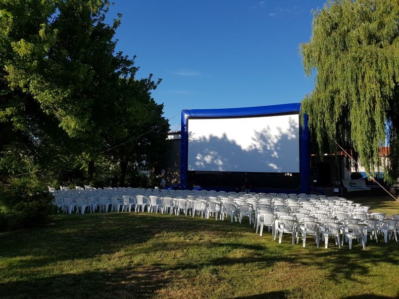 Das Foto zeigt eine große Leinwand mit Stühlen für ein Freilichtkino
