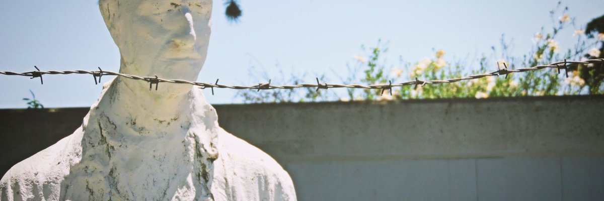 Foto einer menschlichen Skulptur hinter Stacheldraht