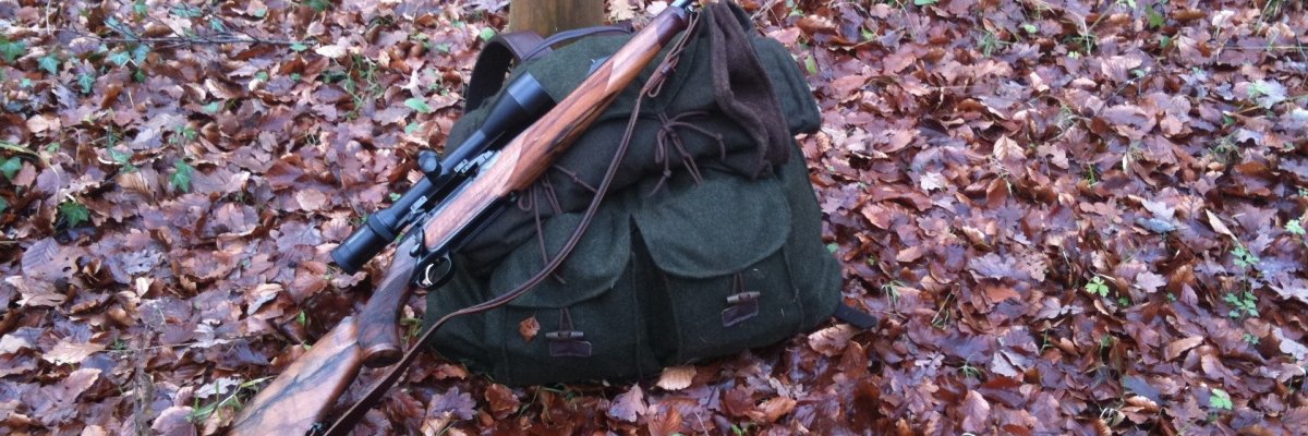 Foto eines Gewehres, das auf einem Rucksack im Laub liegt