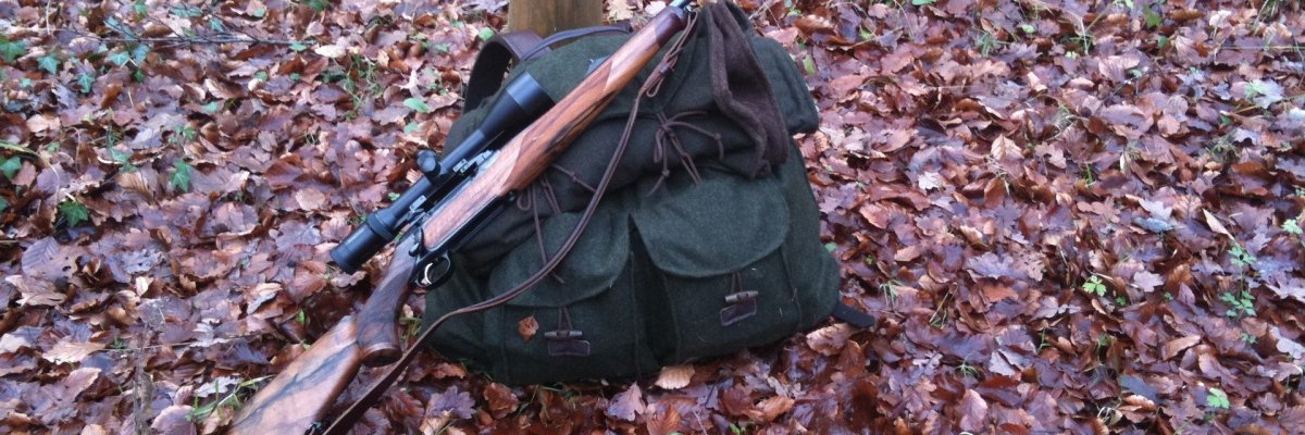 Foto eines Gewehres, das auf einem Rucksack im Laub liegt
