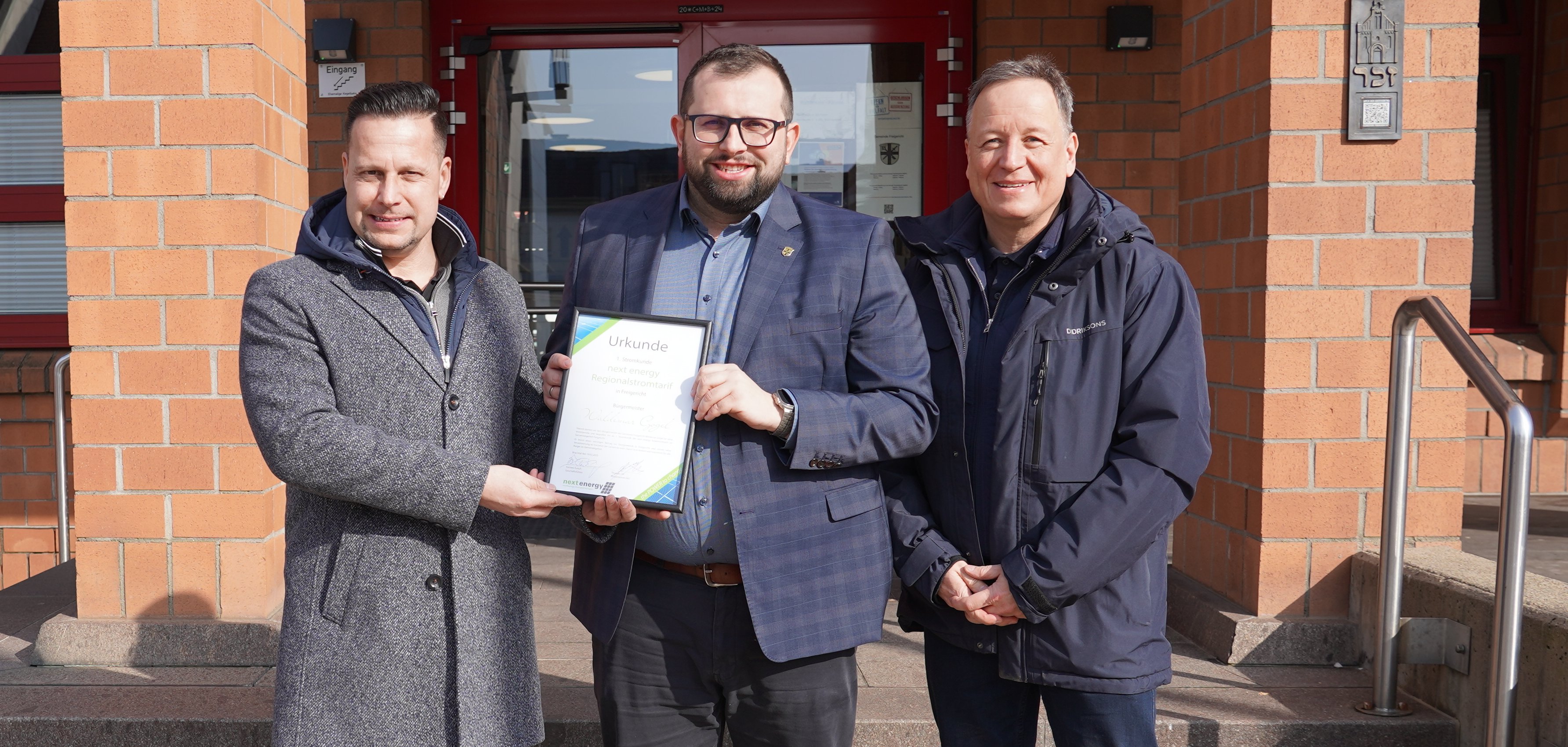 Bürgermeister Waldemar Gogel ist der erste Stromkunde des Next Energy Solarstromtarifs im Gemeindegebiet Freigericht. Torsten Eurich und Thomas Ott von Next Energy überreichten eine Urkunde.