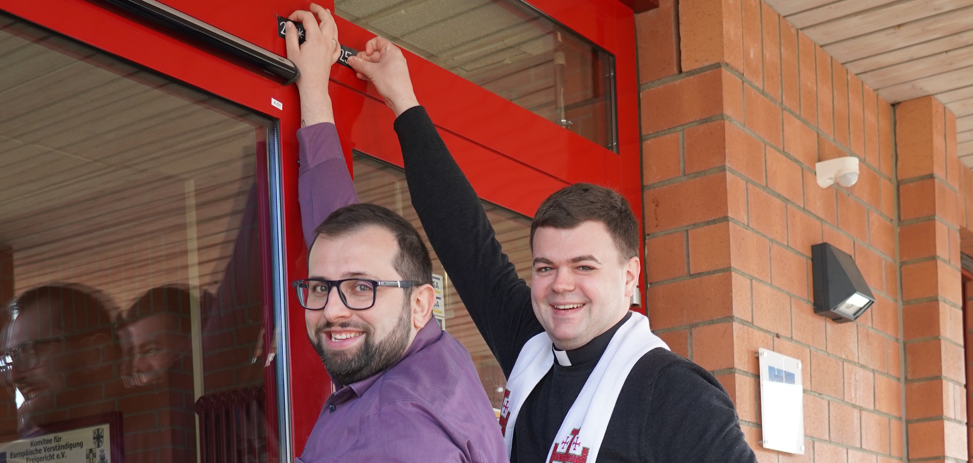 Bürgermeister Waldemar Gogel und Kaplan Johannes Wende bringen das Segenszeichen über der Rathaustür an. 