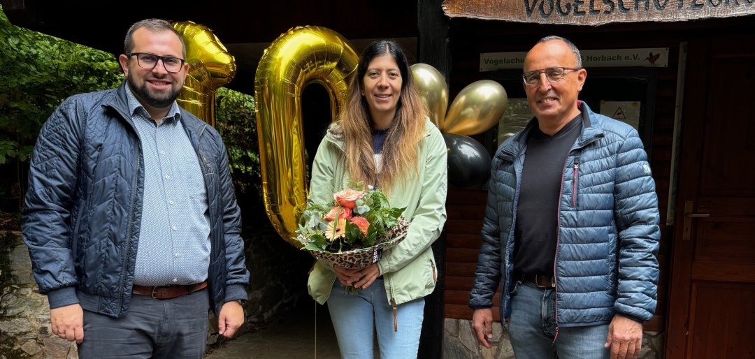 Bürgermeister Waldemar Gogel, Sabrina Schneider mit Blumen und Ordnungsamtsleiter Peter Betz freuen sich über das Jubiläum