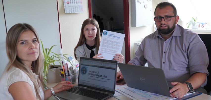 Bürgermeister Waldemar Gogel, Kämmerin Tina Ruzsicska und Auszubildende Loresa Shabani präsentieren die neue Broschüre „Haushalt transparent“.